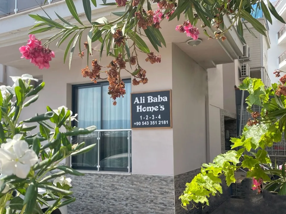 Bina girişindeki 'Ali Baba Home's 1·2·3·4' tabelası ve çiçekler
