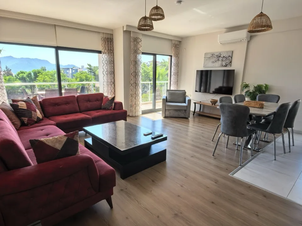 Daire D4'ün salonu — bordo köşe koltuk ve dağ manzaralı balkon