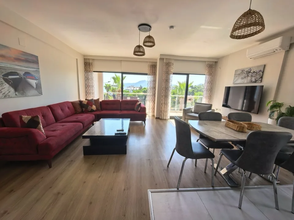 Salon ve yemek alanı — hasır avizeler, televizyon ve balkon kapıları