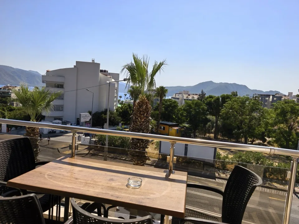 Balkonda ahşap yemek masası, palmiyeler ve arkada deniz