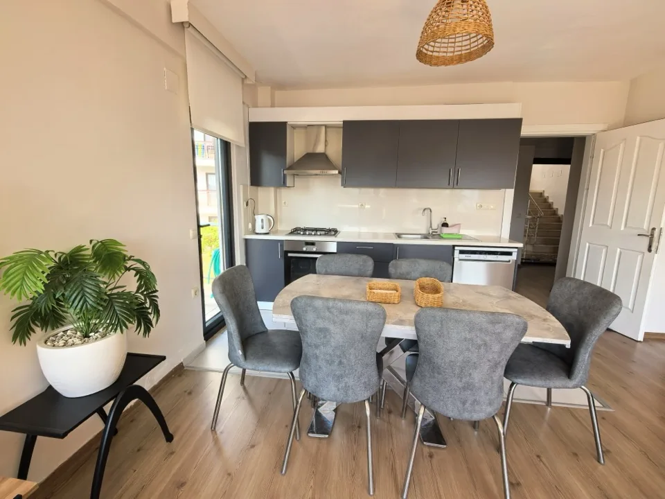 Yemek masası ve altı sandalye, arkada mutfak tezgâhı